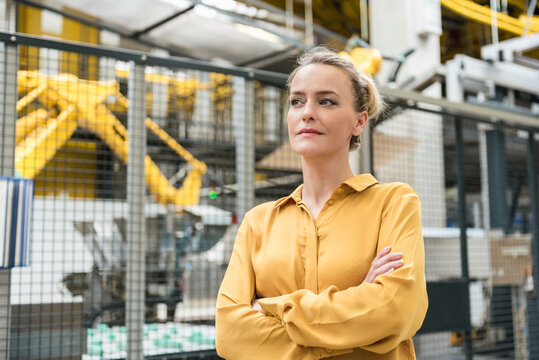 Portrait of confident woman in factory shop floor with industrial robot