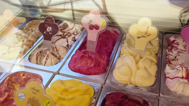 Various colorful ice cream flavors arranged in metal trays inside commercial freezer display, dessert shop and food retail concept.