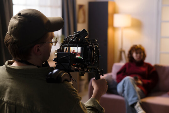 Cameraman films a woman sitting on a couch indoors