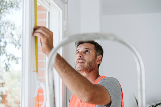 Maintenance engineer measuring window length at house under renovation