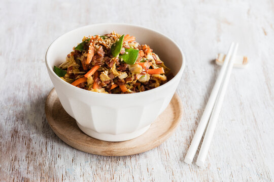 Chopsticks and bowl of fried red rice with vegetables