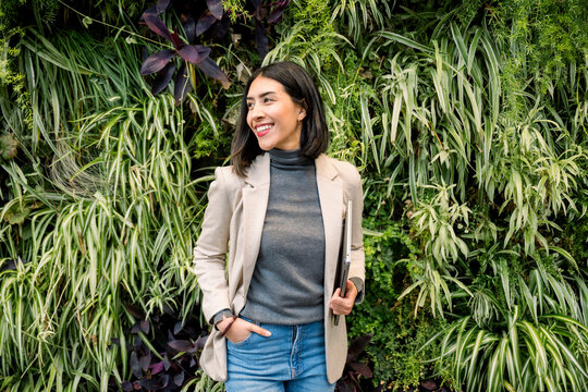 Confident businesswoman in casual outfit holding laptop outdoors