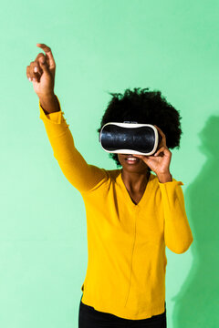 Young woman using virtual reality simulator standing with hand raised against green background