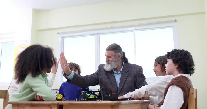 Teacher and students celebrate success with a high five after a STEM robotics activity in the classroom. Back to school concept with teamwork, achievement, learning and inspiration