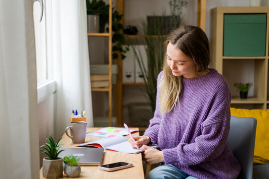 Woman studying and writing in notebook at home with natural light