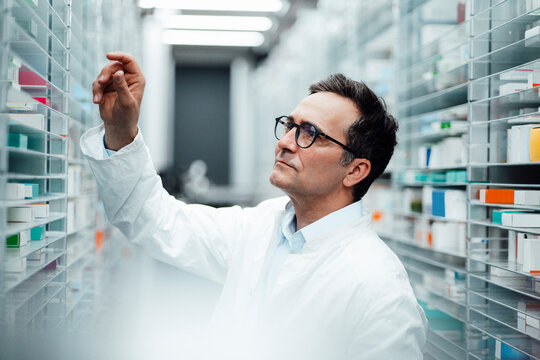 Pharmacist checking medicines on shelf in storage room at pharmacy