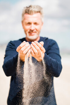Smiling man with sand falling from hands at beach