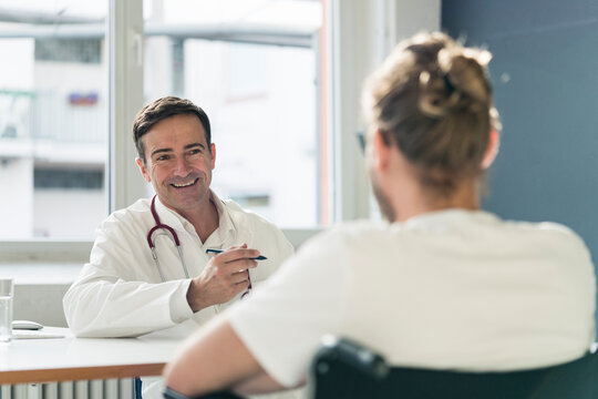 Smiling doctor talking to patient in wheelchair in medical practice