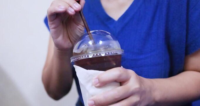 Hand holding an iced black coffee Americano in a plastic takeaway cup with ice. Ideal for cafe, beverage, refreshment, and lifestyle concepts
