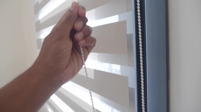Close up hand pulling white bead chain to adjust window zebra blinds