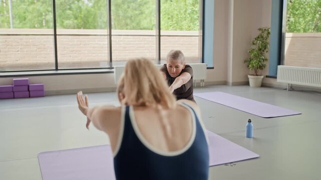 Caucasian women of different ages practicing yoga in studio, stretching arms in circular motions. Ideal for marketing active aging, wellness programs, and healthy lifestyle