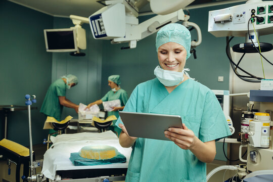Smiling female surgeon in surgery room looking at digital tablet