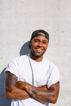 Portrait of laughing young man with arms crossed standing in front of concrete wall