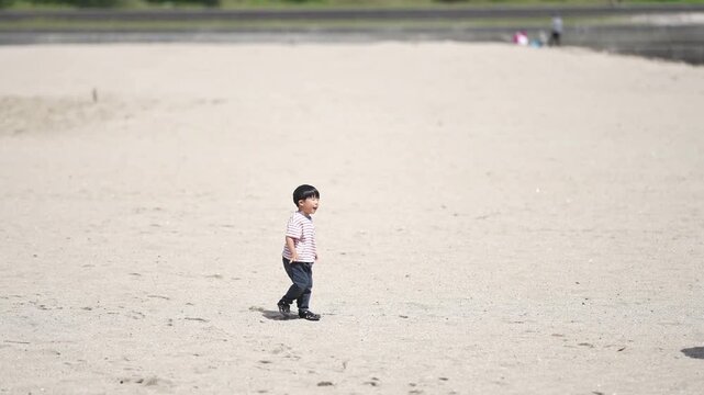 Child digs sand, adult walks nearby. Bright sun, open beach, quiet atmosphere. Child curious, adult calmly observing. Perfect for family, leisure, outdoor moments