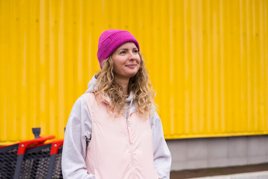 Smiling woman in pink beanie standing outside yellow supermarket