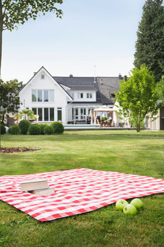 A picnic blanket with a book and apple lies on the grass near a villa