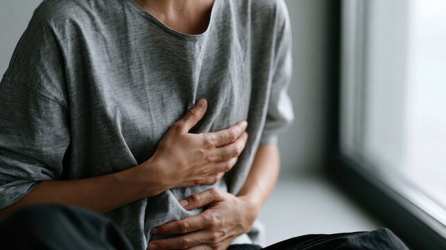 A person is holding their stomach in pain, illustrating a common discomfort or illness. The focus is on the hands covering the abdomen, suggesting internal discomfort or a stomach ache.