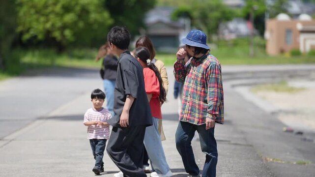 Warm sunlight glows on a quiet suburban street. Family strolls casually, heads down, hands in pockets. One child walks beside a small, steady step. Adults smile subtly, eyes looking ahead