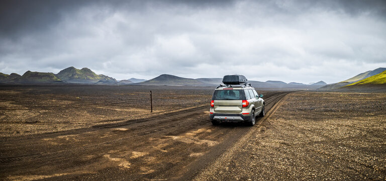 A lone car drives on a dirt road through the Icelandic Highland