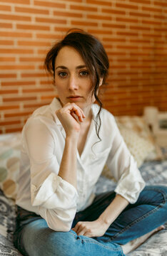 Beautiful female brunette with hand on chin sitting at home