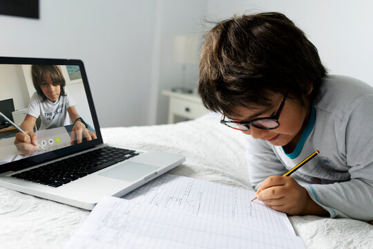 Little boy lying on bed using laptop for video chat