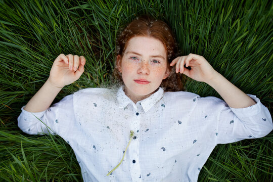 Female with red hair lies in the green grass looking at camera