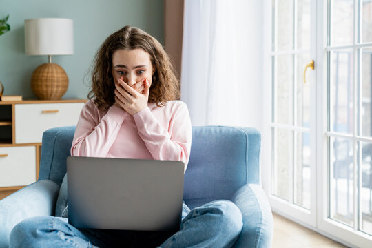 Young freelancer covering mouth with hands looking at laptop