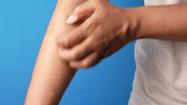 Close up of man scratching itchy skin on his forearm against blue background