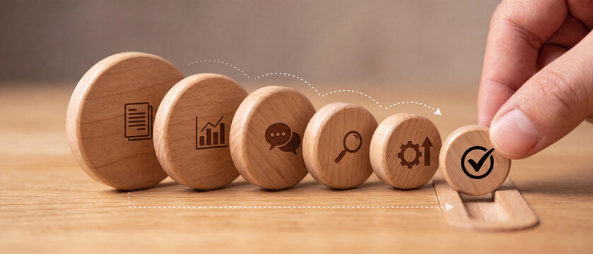 Hand placing the final wooden block with a check mark icon, completing a business process sequence on a wooden table