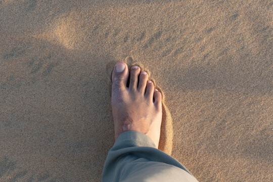 A high-angle first person POV shot of a traveler's single foot standing on the soft, golden sand dunes at the Inland Sea, Khor Al Adaid, Qatar during a desert safari.