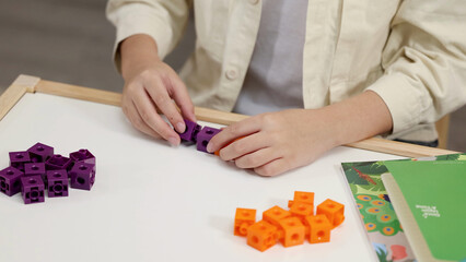 Child Connecting Purple and Orange Math Manipulative Blocks on White Tabletop