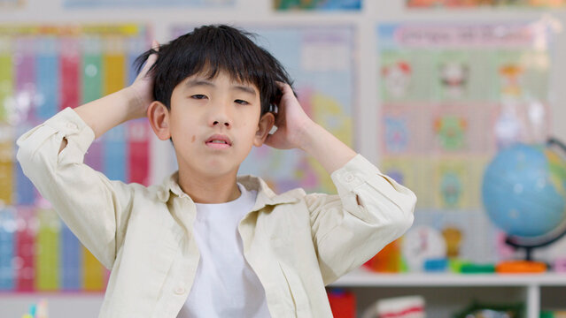 Stressed Asian Boy Holding Head in Frustration Inside a Classroom
