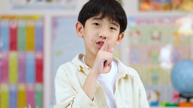 Young Asian Boy Making Shushing Silence Gesture in a Bright Classroom Setting