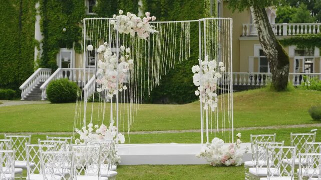 Beautiful wedding ceremony setup featuring a floral arch and white chairs arranged on a lush green lawn, creating a romantic atmosphere