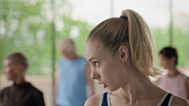 Young adult Caucasian female instructor performing neck stretching exercises in slow motion during group fitness class. Ideal for promoting active aging and wellness programs