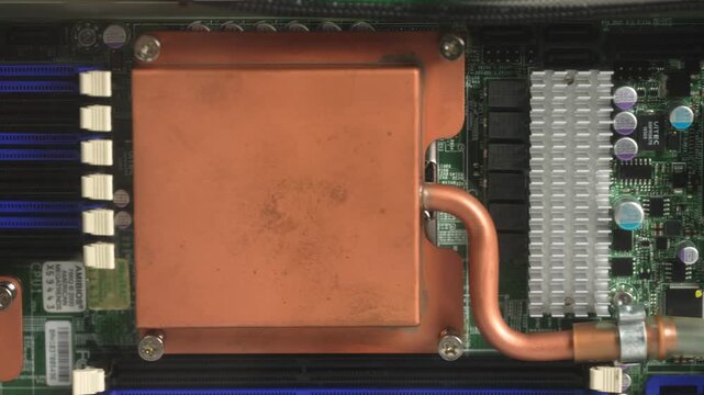 Close-up reveal of server motherboard showing large copper CPU cold plate, heat pipes, aluminum heatsink fins and blue RAM slots in active liquid cooling setup