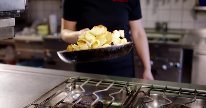 Cook frying golden potato slices in a pan over a gas flame