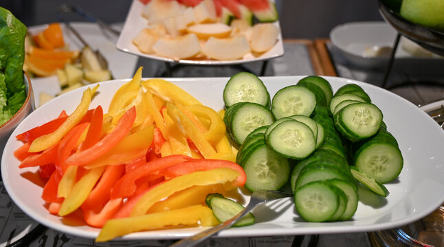 Colorful plate with sliced red and yellow bell peppers and cucumber rounds. Fresh salad served in restaurant. 
