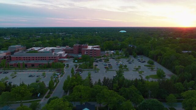 High angle drone flight over a large brick hospital and medical campus surrounded by a dense forest of trees during twilight in Highland Park, Illinois.
