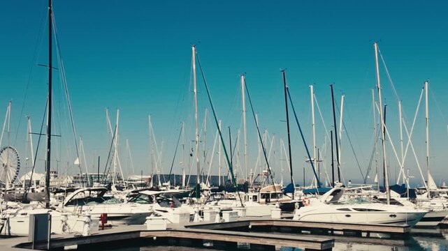 Piers full of docked sailboats on a summer day with a helicopter and Ferris wheel in the background.