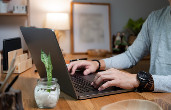 Close up of man hands typing on laptop keyboard on wooden desk.