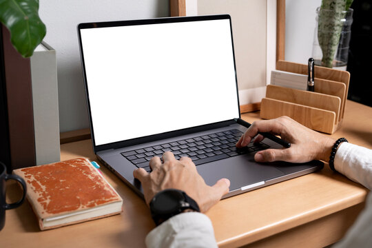 Man working on laptop with blank white mockup screen on wooden desk.