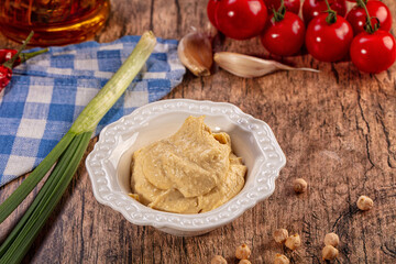Fototapeta premium Creamy Hummus Bowl with Fresh Ingredients on Rustic Wood Table