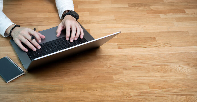 Man hands typing on laptop keyboard on wooden table.