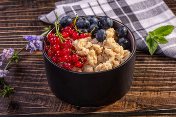 Oatmeal bowl with blueberries and red currants on wooden table © Andrei Starostin