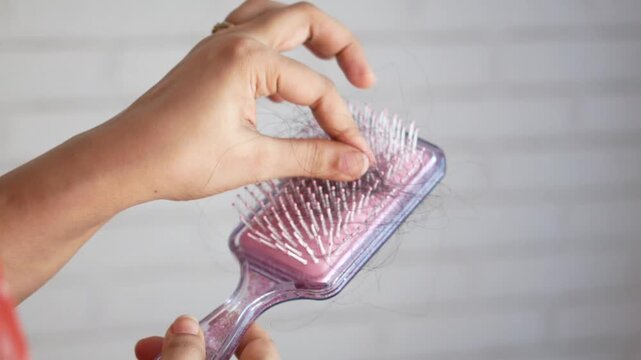Woman removing fallen hair from purple comb against white brick wall background in slow motion clip