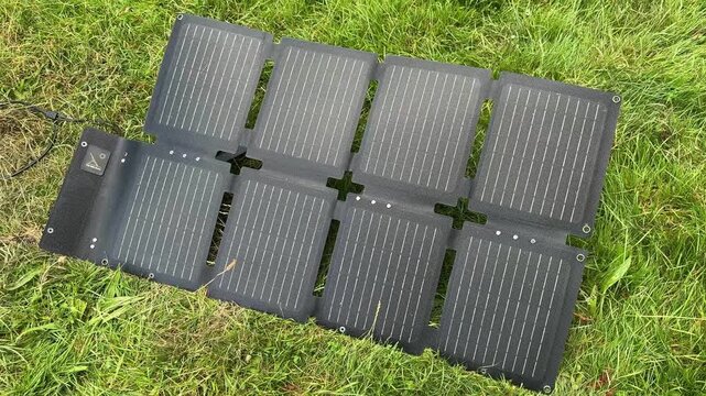Portable foldable solar panels on grass generating clean renewable energy. Concept of off-grid power, sustainable technology, camping, eco-friendly travel and portable electricity.