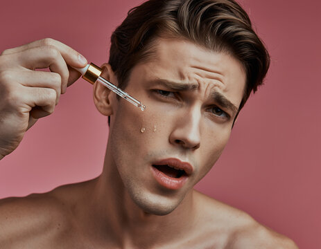 Studio Portrait Of Handsome Man Applying Skin Care Oil From Glass Pipette