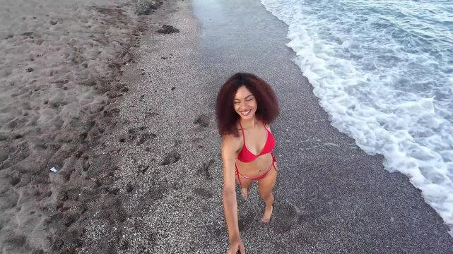 Young Black wonan travel content creator filming authentic UGC destination experience on tropical beach, waving and looking to the camera, summer vacation lifestyle, tourism promotion and paradise