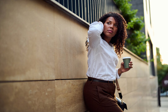 African American Businesswoman Leaning on Urban Wall Holding Coffee Cup, Thoughtful and Confident